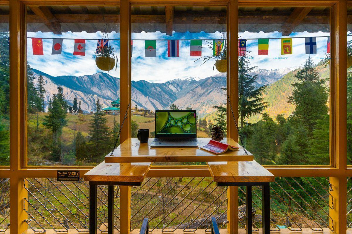 Digital nomad working on a laptop from a mountain cabin in Himachal Pradesh with panoramic Himalayan views.